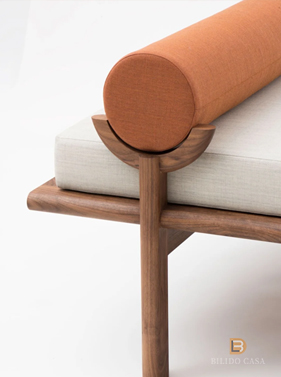 Custom seating detail with orange cylindrical accent and wooden frame, merging upholstery and structural design.